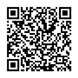 一个身穿套装的群众演员在展台布景里露了一面二维码生成